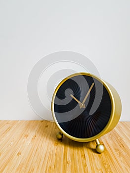 A shining black watch with a gold frame stands on a wooden table