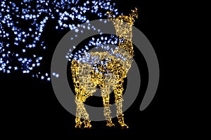 a Shining deer made of lots of yellow lights stands in the garden behind a tree decorated with blue lamps in the night