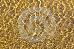 Shining reflections of sun rays on rock bottom and ripples on the water surface.