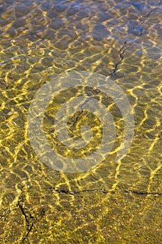 Shining reflections of sun rays on rock bottom and ripples on the water surface.