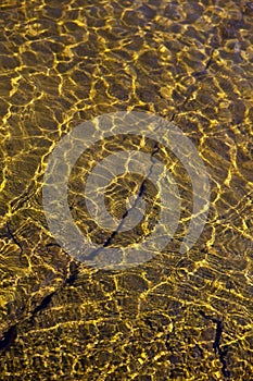 Shining reflections of sun rays on rock bottom and ripples on the water surface.