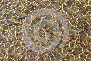 Shining reflections of sun rays on rock bottom and ripples on the water surface.