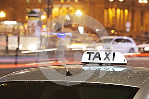 Shining Taxi inscription close up against passing cars on night street