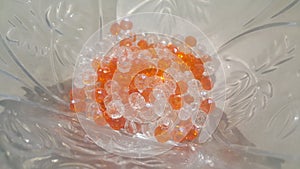 Shining, transparent, orange color crystal beads or gemstones in a glass bowl