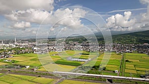 Shinkansen passes green rice fields at foot of Mt. Fuji on summer day