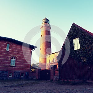 Shinning old lighthouse above houses before sunset. Tower illuminated with strong warning light