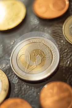 Shiny 2 euro coins and some others around, close up on a glass table