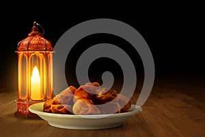 Shiny arabic lantern and bowl of fresh dried date on wooden floor at night