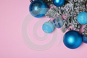 Shiny blue Christmas balls and fir tree branches with snow on pink background, flat lay. Space for text