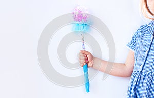 Shiny blue magic wand in the hand of a girl in plaid dress on light background faceless with copy space. Happy birthday