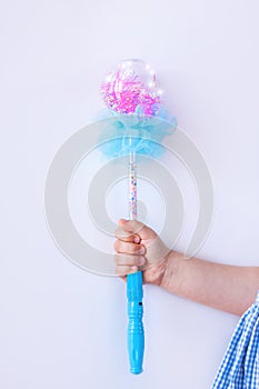 Shiny blue magic wand in the hand of a girl in plaid dress on light background faceless with copy space. Happy birthday