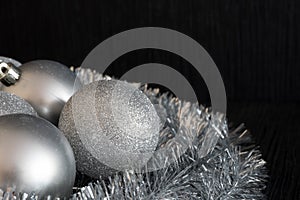 Shiny and bright silver christmas balls decoration lying on silver christmas chain on dark black structured background. Detail or