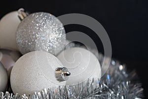 Shiny and bright white christmas balls decoration lying on silver christmas chain on dark black structured background. Decoration
