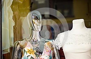 Shiny chrome mannequin dummy standing in a store window display with other mannequins in the background