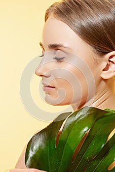 Shiny. Close up of beautiful female face with green leaves over white background. Cosmetics and makeup, natural and eco