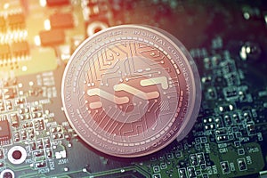 Shiny copper NXT cryptocurrency coin on blurry motherboard background