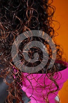 Shiny curly hair falling into a pink blow dryer with a blue background