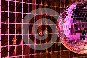 Shiny disco ball against foil party curtain under pink light, space for text