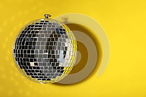 Shiny disco ball on yellow background, top view. Space for text