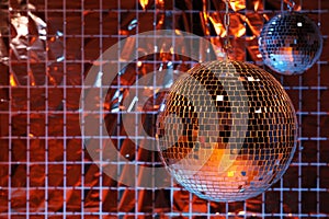 Shiny disco balls against foil party curtain under color lights, space for text