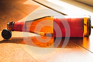 Shiny empty beer bottle lying down on wooden floor in natural light