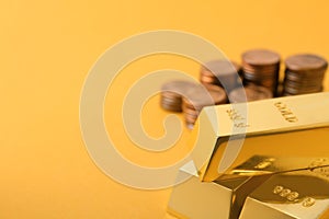 Shiny gold bars and coins on color background.