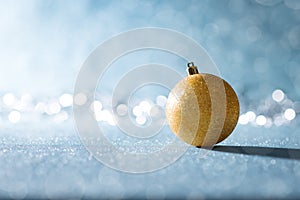 Shiny Gold Christmas Bauble in Winter Wonderland. Blue Christmas background with defocused christmas lights.