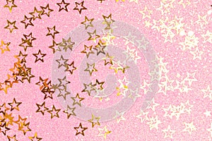 Shiny gold colored glittering stars confetti on a pink background.