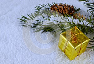 A shiny gold present laying in snow next to a pine bough.
