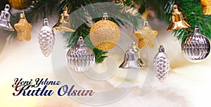 Shiny gold and silver christmas balls, stars and bells on white with pine tree. Yeni yiliniz kutlu olsun means happy new year