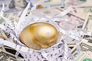 Shiny golden egg in paper nest with financial numbers on pile of US dollar banknote money metaphor of finding the good stock with