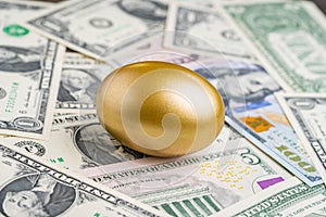 Shiny golden egg on pile of US America dollar banknotes money metaphor of finding the unbelievable good stock with high dividend