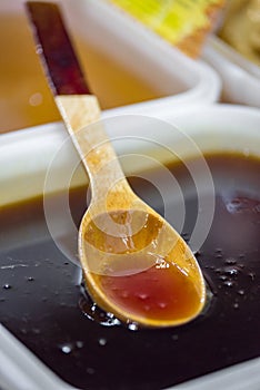 Shiny golden honey dripping off of a wooden spoon into a plastic bowl.