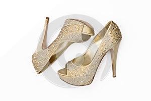 Shiny golden shoes with high-heeled stones on a white background