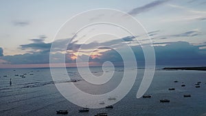 Shiny golden sunset with yellow sky and sun rays through grey clouds reflecting on calm lagoon with anchored boats in