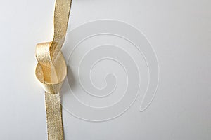 Shiny golden textile ribbon with knot on white background