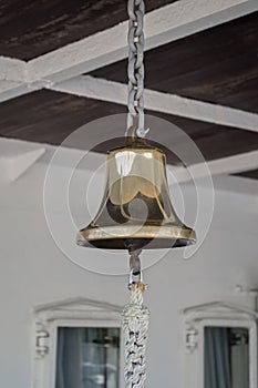 Shiny goldish ship bell hanging on chain with tongue ending in hook with attached braided rope. Bulkheads of  lower upper deck. photo