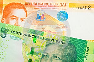 A shiny, green 10 rand bill from South Africa paired with a orange and white twenty piso note from the Phillipines.