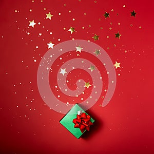 Shiny green little gift on a red background with sparkles of gold stars.