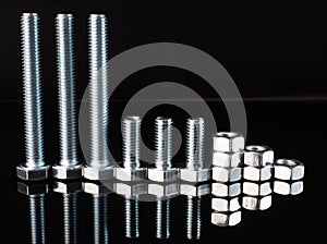 Shiny metal bolts and nuts of different sizes on a black mirror background