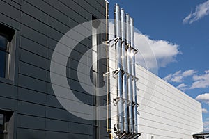 Shiny metal chimney on the outer wall of industrial building against a blue sky background.