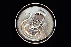 Shiny metal cola can lid with water drops on black background. Golden bottle of drink, lid of packaging of beer. Top view