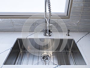 A shiny, metal sink faucet on a beautiful, marble countertop in a high-end kitchen