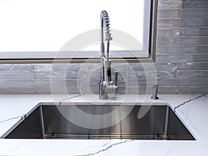 A shiny, metal sink faucet on a beautiful, marble countertop in a high-end kitchen