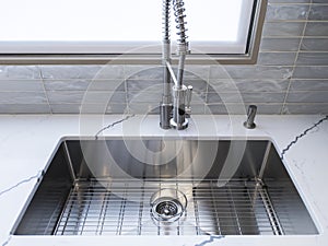 A shiny, metal sink faucet on a beautiful, marble countertop in a high-end kitchen