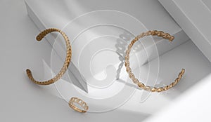 Shiny Modern gold braid shape and chain shape bracelets and ring on white geometric background
