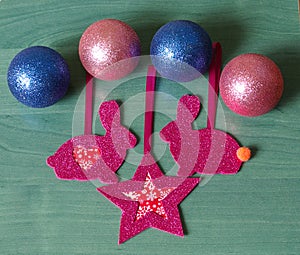 Shiny pink Christmas tree decorations in the shape of a rabbits, star and Christmas balls on a green background
