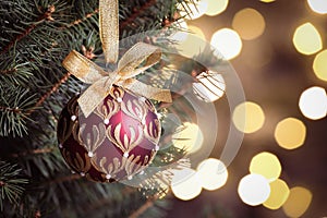 Shiny red ball hanging on Christmas tree against festive lights, closeup. Space for text