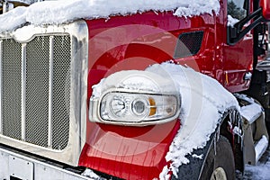 Shiny red big rig semi truck tractor standing for truck driver rest on the winter truck stop parking lot with snow and ice