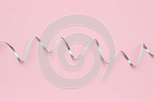 Shiny silver ribbon streamers serpentine on pink background in minimal style. Concept decorations for celebration, party, holiday